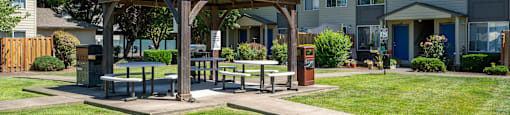 A gazebo is surrounded by a grassy area in front of apartment buildings.