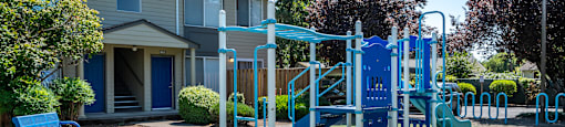 A playground with a blue slide and a blue bench in front of a building.