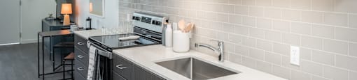 1 BR Apartments in Eugene OR - Crosswood Apartments - Modern Kitchen with Wood-Style Cabinetry, White Countertops, Stainless Steel Appliances, and a Small Dining Area