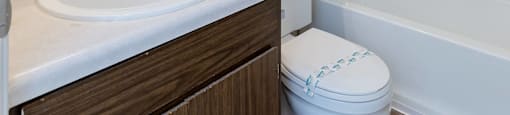 A white toilet with a brown cabinet and a white sink with a mirror above it.