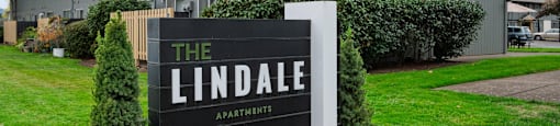 A sign for The Lindale Apartments stands in front of a grey building.