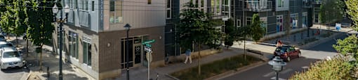 A street view of a city with a building on the left and a car driving on the road.