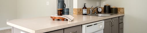 A kitchen with a white counter top and grey cabinets.