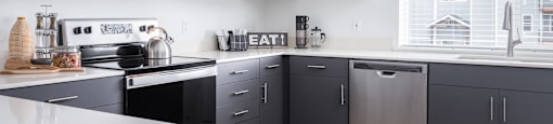 2 BR Apartments in Oregon City OR - Timberview Apartments and Townhomes - Bright Modern Kitchen with a Large Window, Stainless Steel Appliances, White Quartz Countertops, and White and Dark Grey Cabinetry