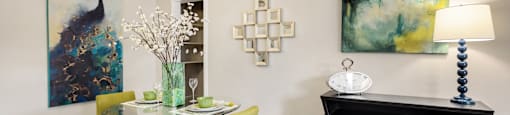 A dining room with a table set for two and a painting on the wall.