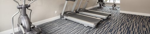 A gym with a row of treadmills and a stationary bike.