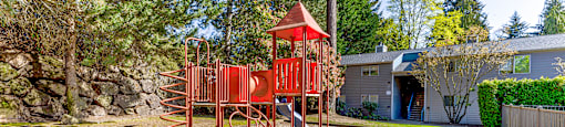 A playground with a red swing set in the middle of a gravel area.