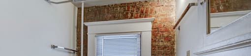A white bathroom with a brick wall and a window.