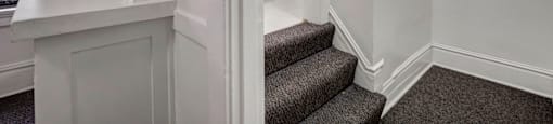 A staircase with a carpeted runner and a white wall.
