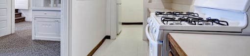 A white kitchen with a stove and a doorway leading to another room.