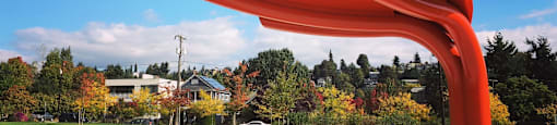 A large red sculpture resembling a chair stands in a park.