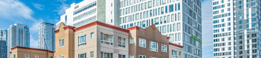 A brown building with a red roof is in the foreground with cars parked in front.