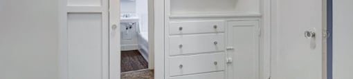 A white cabinet with drawers is open to a bedroom.