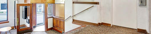 A hallway with a bench, a staircase, and a door with a sign on it.