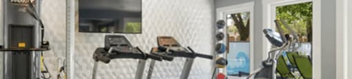 A treadmill and other exercise equipment are in a well-lit room.