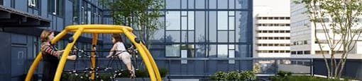 A playground with a yellow slide is in front of a tall building.