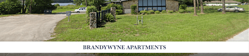 A sign for Brandywynne Apartments is displayed in front of a building surrounded by trees.