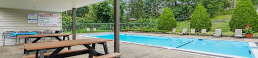 Picnic tables are set up under a white canopy next to a swimming pool.