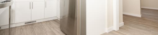 A stainless steel refrigerator stands in a kitchen with white cabinets and a window.