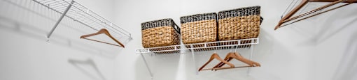 a walk in closet with white walls and shelves with baskets and hangers