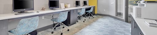 a long desk with computers and chairs in a room with a yellow wall