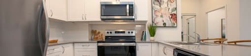 Kitchen with white designer cabinetry and stainless steel fridge, stove, over-the-range microwave and dishwasher at Bayfield Tower Apartments in Barrie, ON