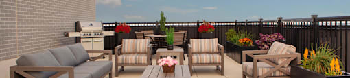 Rooftop terrace with cushioned patio seating and a BBQ seen in the background at Bayfield Tower Apartments in Barrie, ON