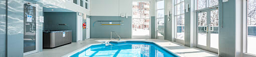 Bourg du Village indoor pool with high ceilings and floor to ceiling windows and patio door leading to outdoor patio area in Sainte Therese, QC