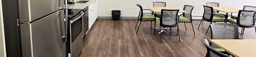 Social room with couch, tables, chairs, and stainless steel appliances at Brockville Apartments in Brockville, ON