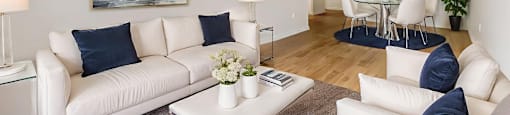 A living room with white furniture and a painting on the wall.