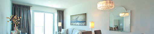 Dining room with set table and a blue table cloth. Living room is behind with a view of the patio at Cityview Apartments in Brampton, ON