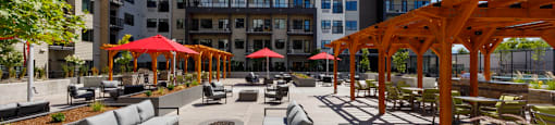 A sunny day at a modern outdoor seating area with red umbrellas and wooden pergolas at The Ambrosi in Kelowna, BC.