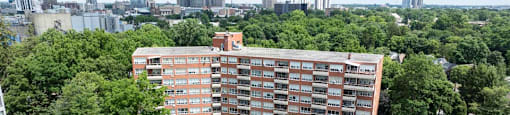 A large red building surrounded by trees with a city in the background.
