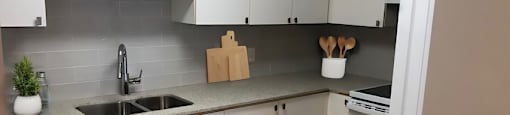 A kitchen with white cabinets and a grey backsplash  at Angus House in Toronto