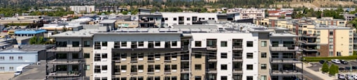 A large white building with a black roof is in the foreground of a cityscape.