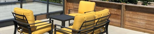 Two yellow chairs are on a patio with a table and a view of the mountains at 388 Kaslo East Village.