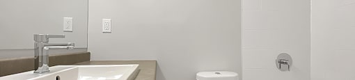 Kensington Apartments bathroom with vanity on left side, toilet in middle and bathtub with shower on right side