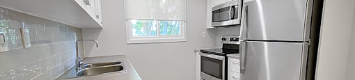 Kensington Apartments in Brockville partially open concept kitchen with stainless steel fridge, stove and OTR microwave
