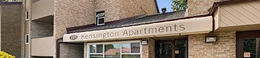 The image shows the front entrance of Kensington Apartments with a clear sky in the background.