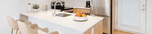 A modern kitchen with a stainless steel refrigerator, sink, and bar stools at 388 Kaslo East Village.