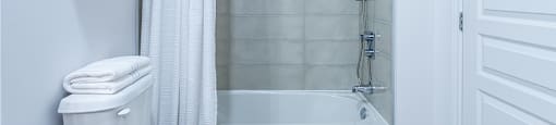 Modern white and grey bathroom featuring a shower tub at La Voile Pointe-Claire apartments in Pointe-Claire, Quebec