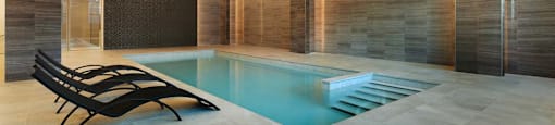 A modern indoor swimming pool with a wooden wall and black lounge chairs.