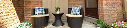 A patio with two chairs and a table with a plant on it.