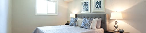 A bedroom with a bed, nightstand, and two pictures on the wall.