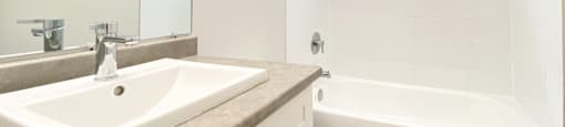 A white bathroom with a sink, toilet, and bathtub at Moira Apartments in Belleville, ON