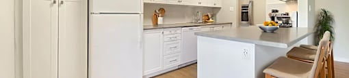 A galley kitchen with white appliances and cabinets and a breakfast bar with seating at Moira Apartments in Belleville, ON