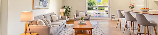 A living room for a two bedroom apartment at Moira Apartments in Belleville, ON with a grey sofa, a wooden coffee table, and a painting on the wall.