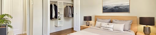 A bedroom with a large bed and a wardrobe with clothes hanging on it at Moira Apartments in Belleville, ON