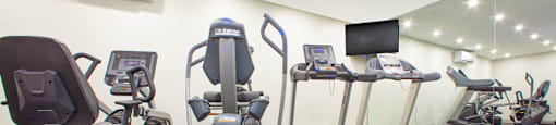 Gym with various cardio machines and a TV at Northgate Tower Apartments in Woodstock, Ontario