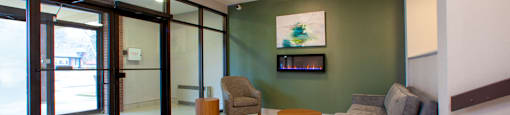 Lobby with a couch, a chair and side tables looking towards entry with floor to ceiling windows and doors at Northgate Tower Apartments in Woodstock, Ontario